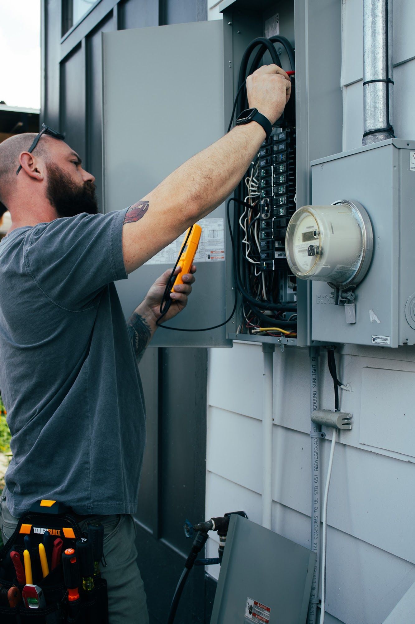 Electrician using a voltage tester on a circuit panel outdoors.