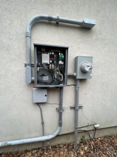 Electrical panel and meter box mounted on a light-colored wall, with gray conduit and a small box below.
