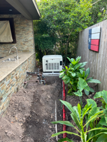 Trench dug for underground wiring near a generator, adjacent to a patio with a sink and a Texas flag on a wooden fence.