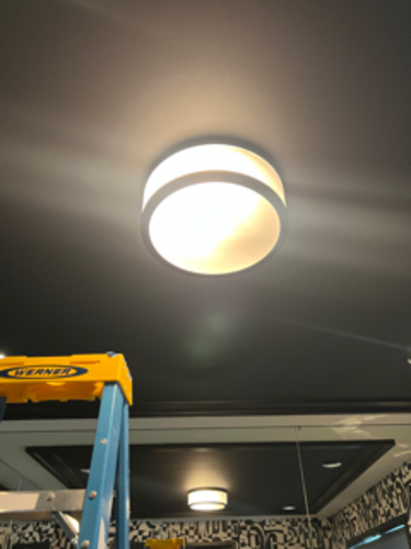 Bright ceiling light fixture against dark ceiling, with a ladder in frame.
