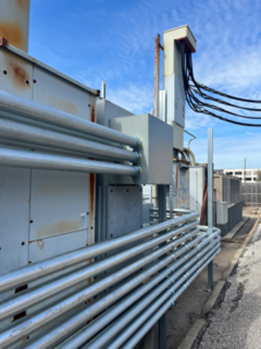 Industrial rooftop equipment with metal pipes, electrical conduits, and wiring against a blue sky.