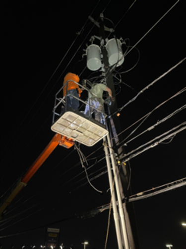 Two utility workers on a lift, working on power lines at night.