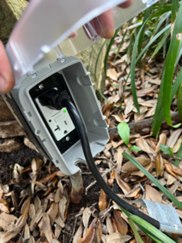 Outdoor electrical outlet with a connected black power cord; ground setting.