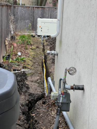 Trench dug next to a building, with yellow pipe visible. Gas meter and generator are also in view.