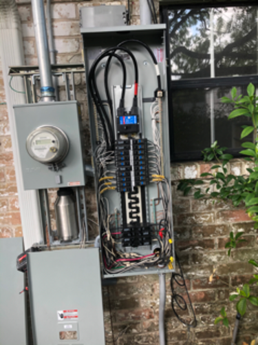 Electrical panel with exposed wiring, next to a meter. Mounted on brick exterior.