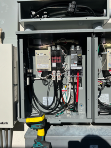Open electrical panel with wires and circuit breakers; a work light sits below.