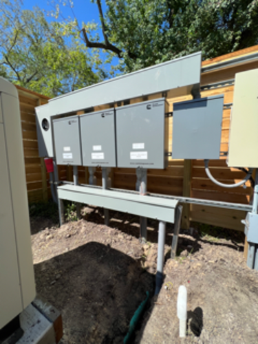 Outdoor electrical boxes mounted on a gray metal frame, next to a wooden fence.