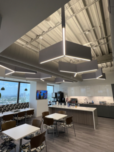 Modern office kitchen with geometric lighting, tables, chairs, coffee machine, and cityscape views.