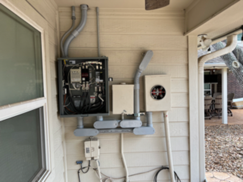 Outdoor electrical panel and meter box mounted on a beige house exterior. Conduit visible.