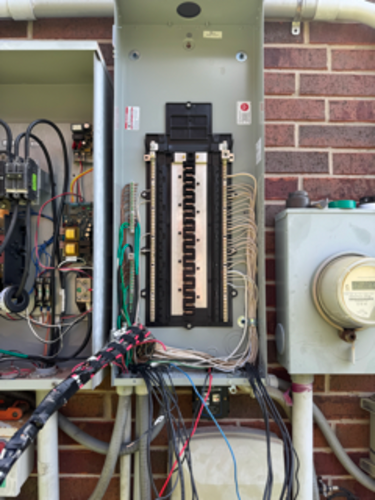 Open electrical panel mounted on a brick wall with exposed wiring and circuit breakers.