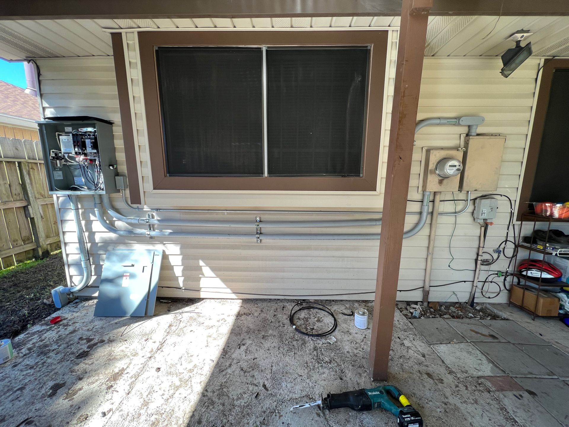 Exterior wall with window, electrical boxes, conduit, and a saw on a wood surface.