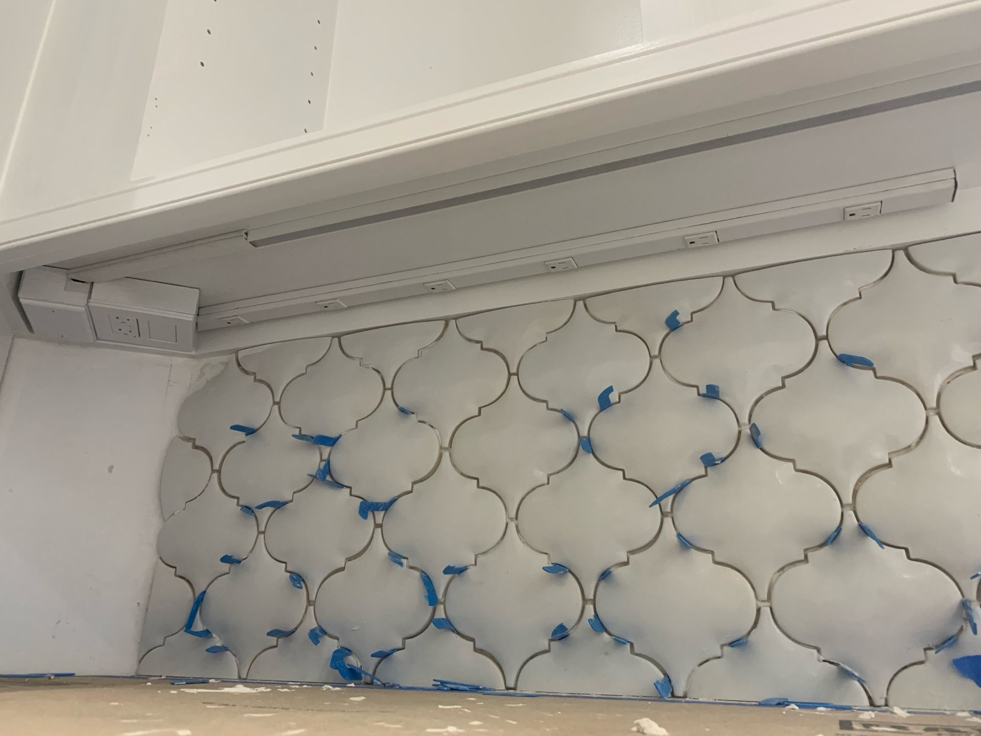 White arabesque tile backsplash under a white cabinet, some blue tape visible.