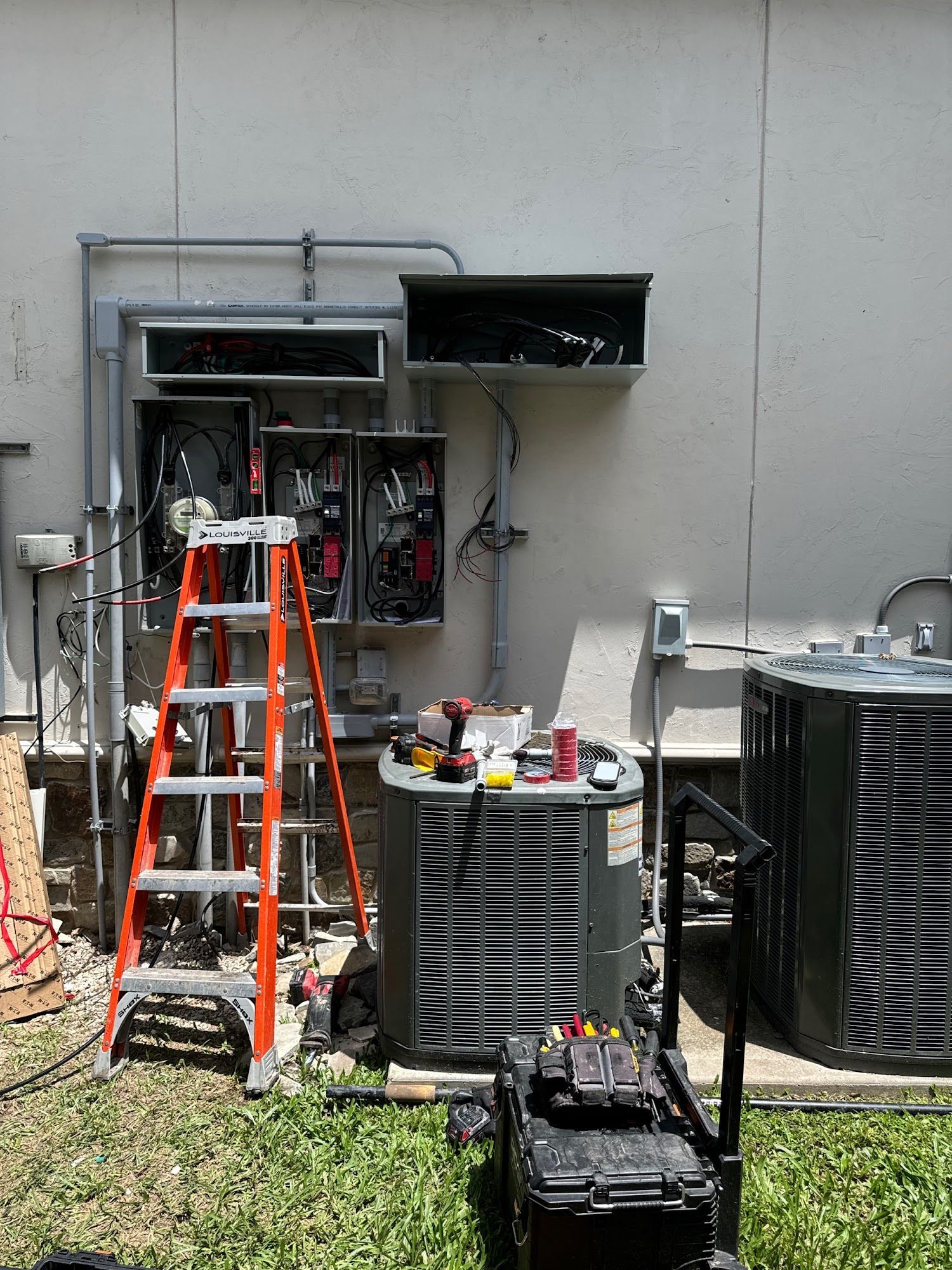 Electrical equipment being worked on outside, with ladder, tools, and air conditioning units.