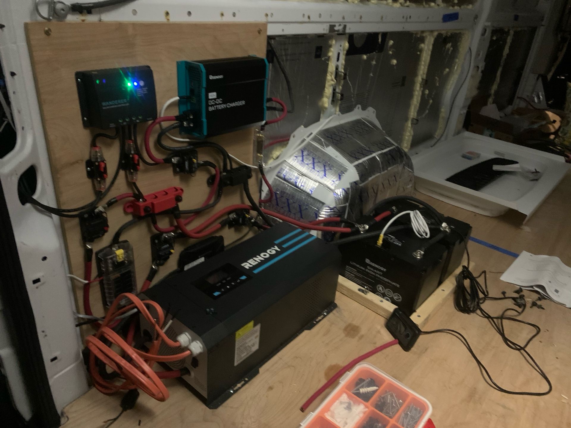 Van electrical system: solar charge controller, inverter, battery bank, and wiring mounted on a plywood panel.