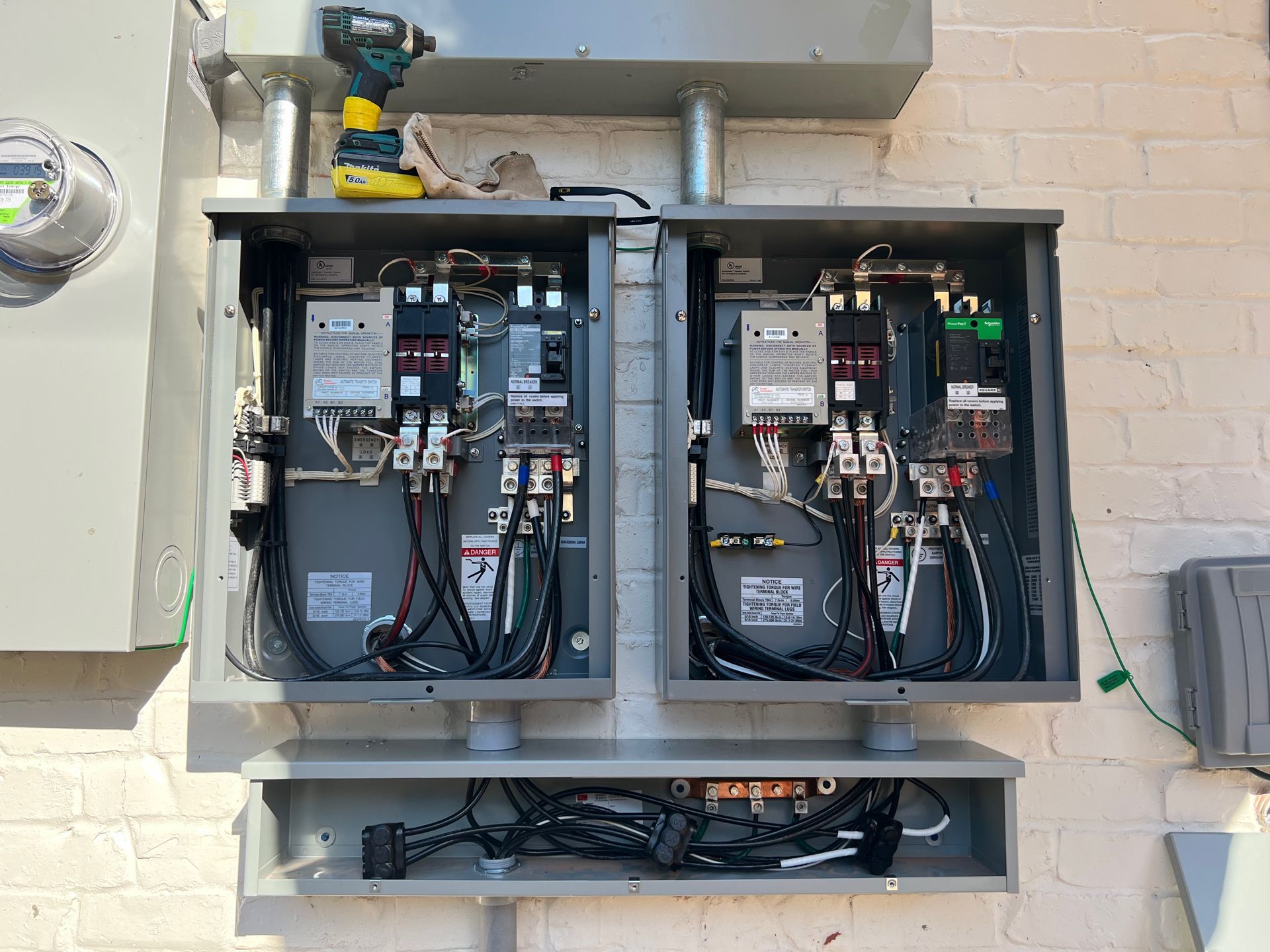 Two open electrical boxes on a brick wall, wires visible. A drill and metal conduit are present.