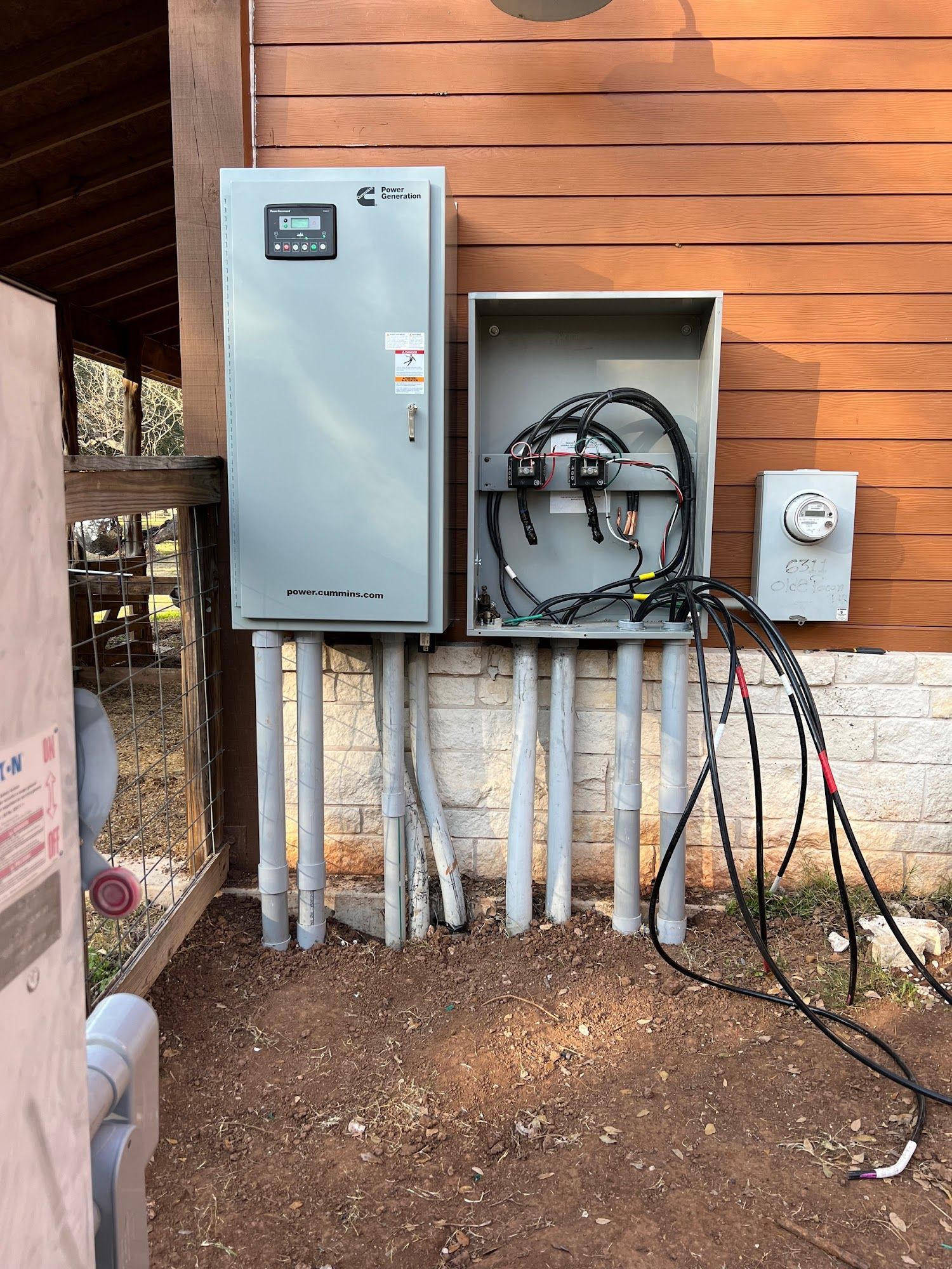 Electrical boxes and meter mounted on a wooden building, with conduit pipes running to the ground.
