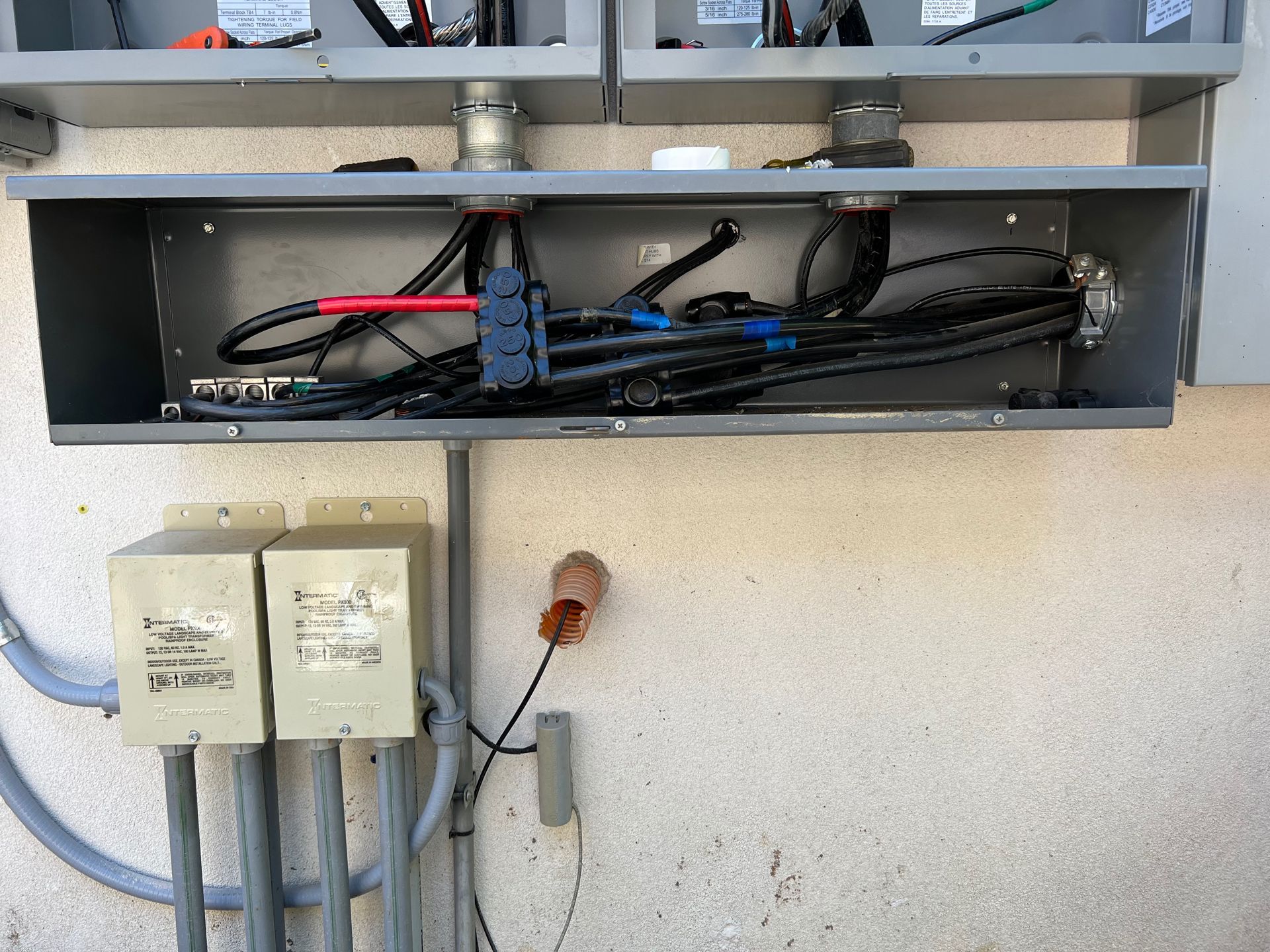 Electrical junction box with cables and conduit mounted on a stucco wall, with two small grey boxes below.