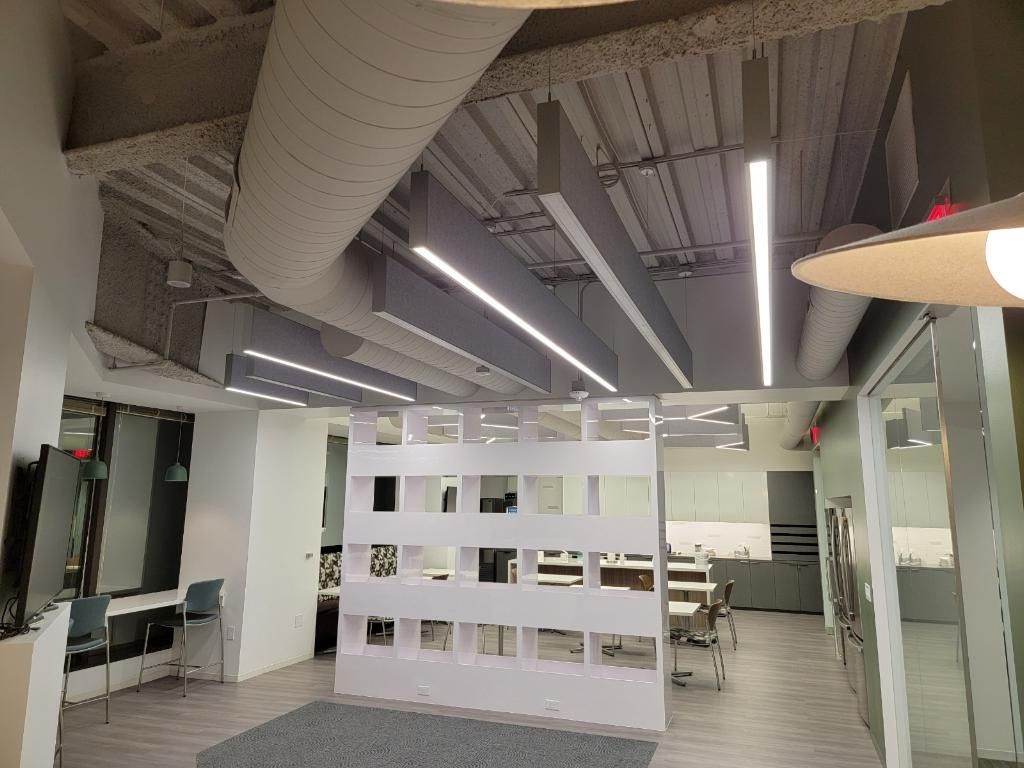 Office interior with open ceiling, linear lights, and a white partition wall.