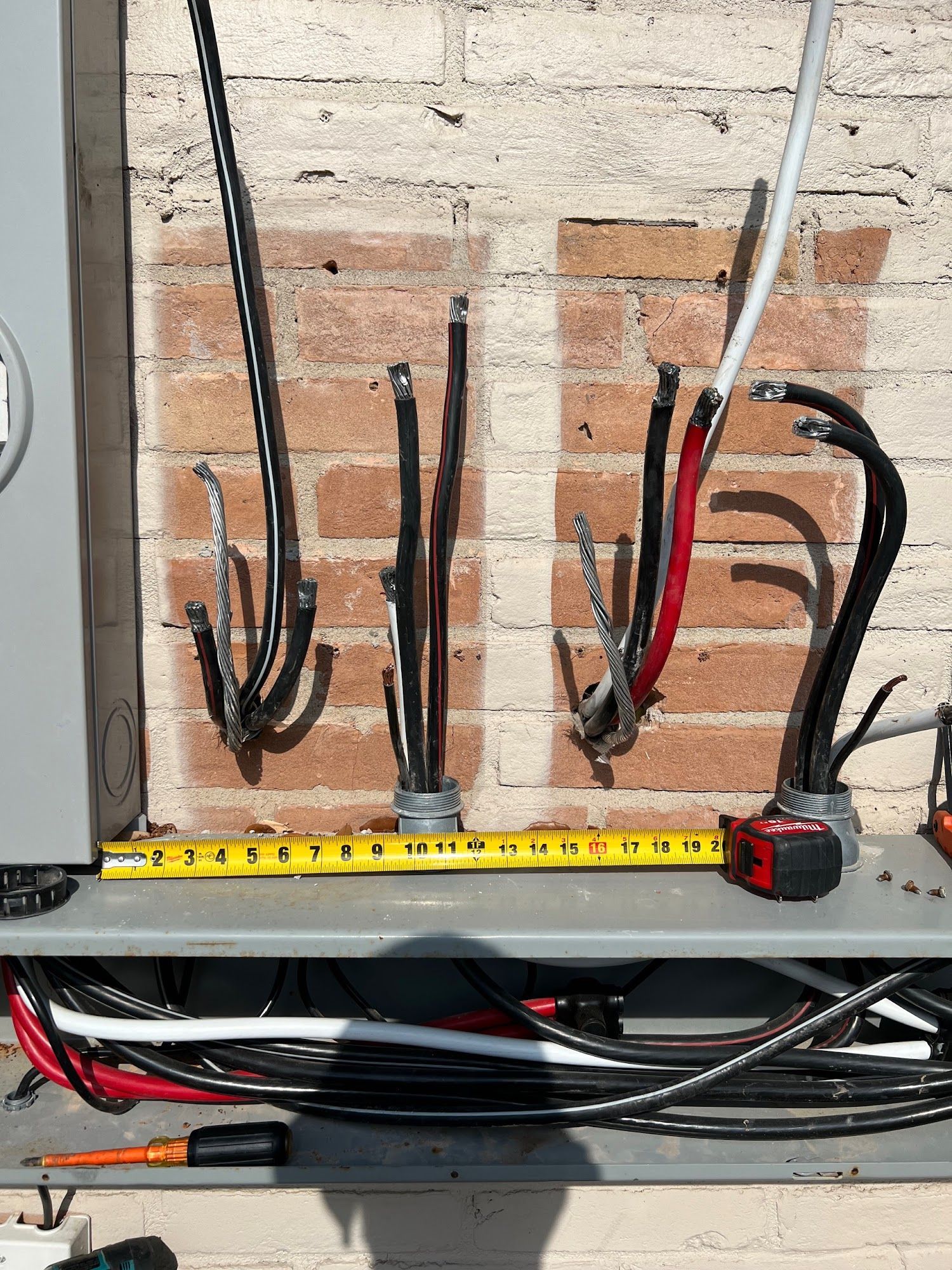 Electrical wires protruding from a metal box on a brick wall; tape measure visible.