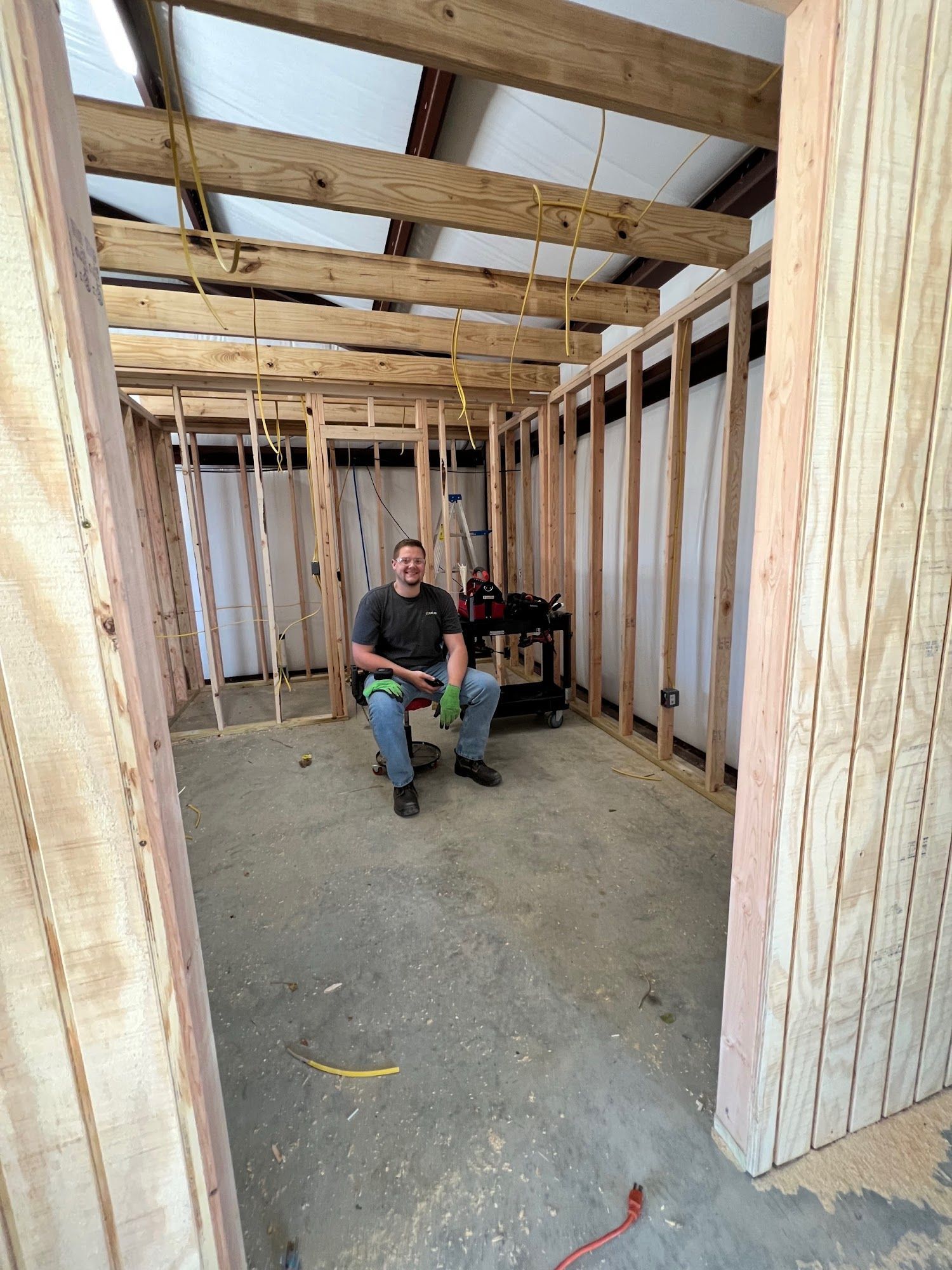 A person sits inside a room under construction, surrounded by wooden framing.