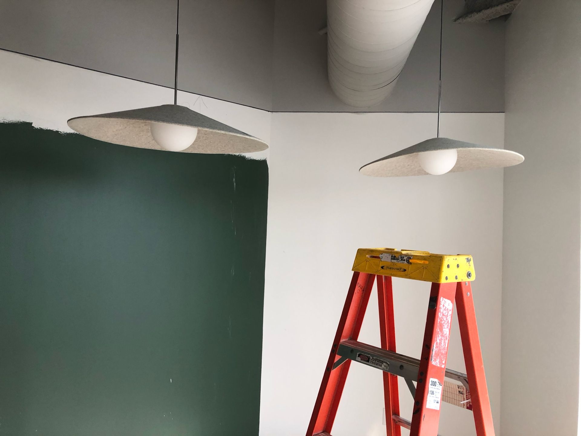Two pendant lights hang in a corner with a partially painted wall, next to a red ladder.