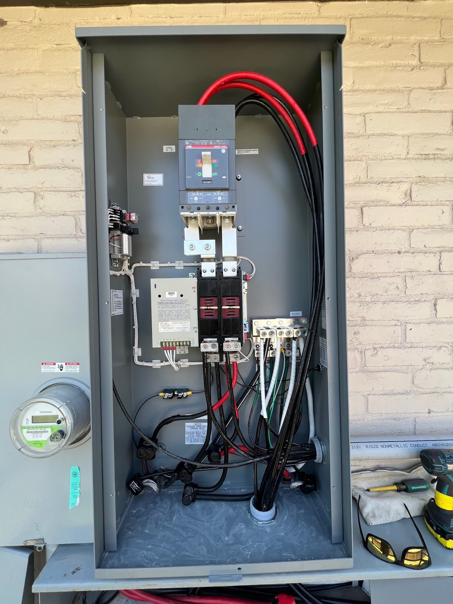 Electrical panel with wires and circuit breakers, mounted on a wall.