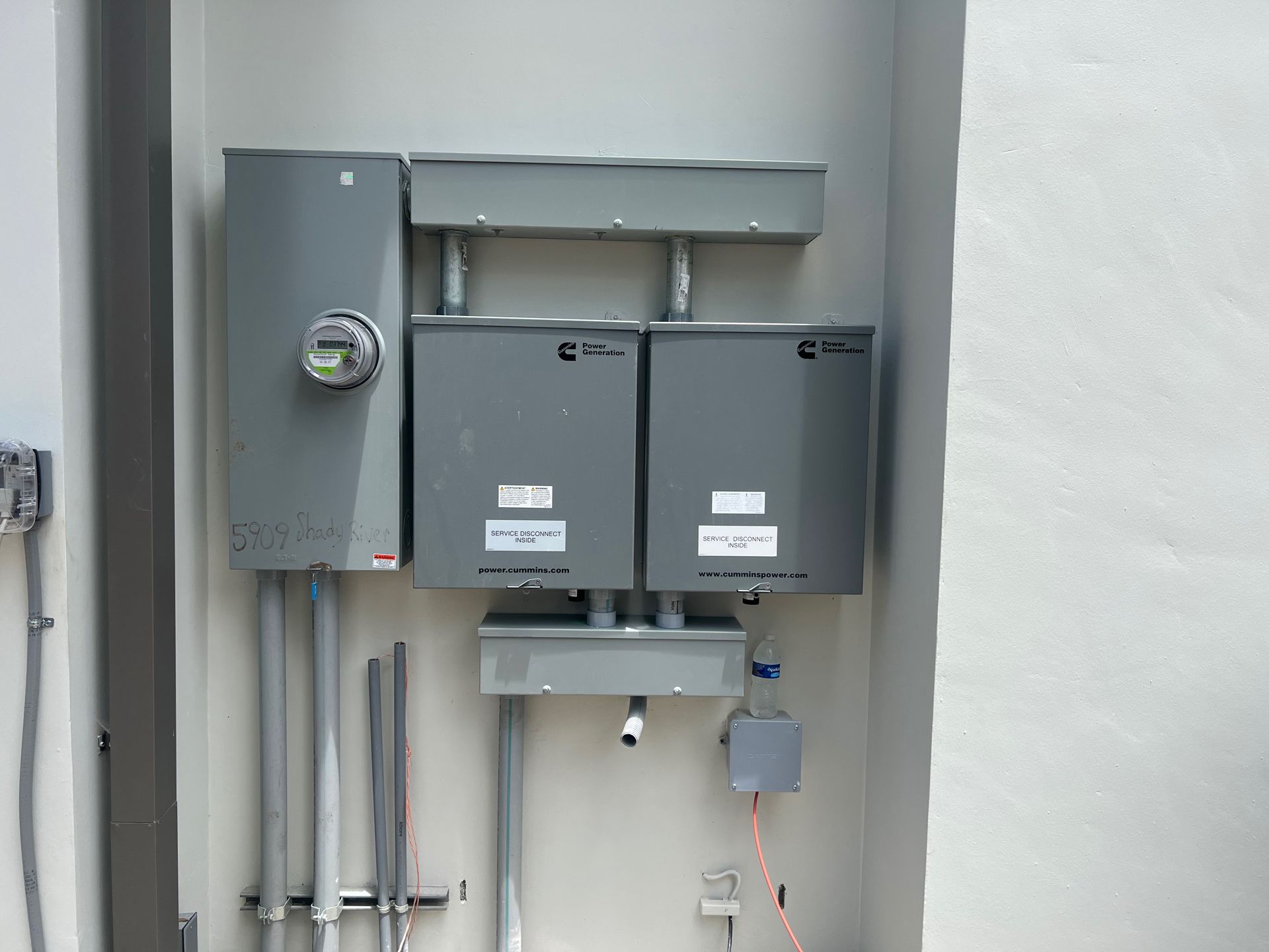 Electrical panel system with meter and two gray boxes mounted on a white wall.