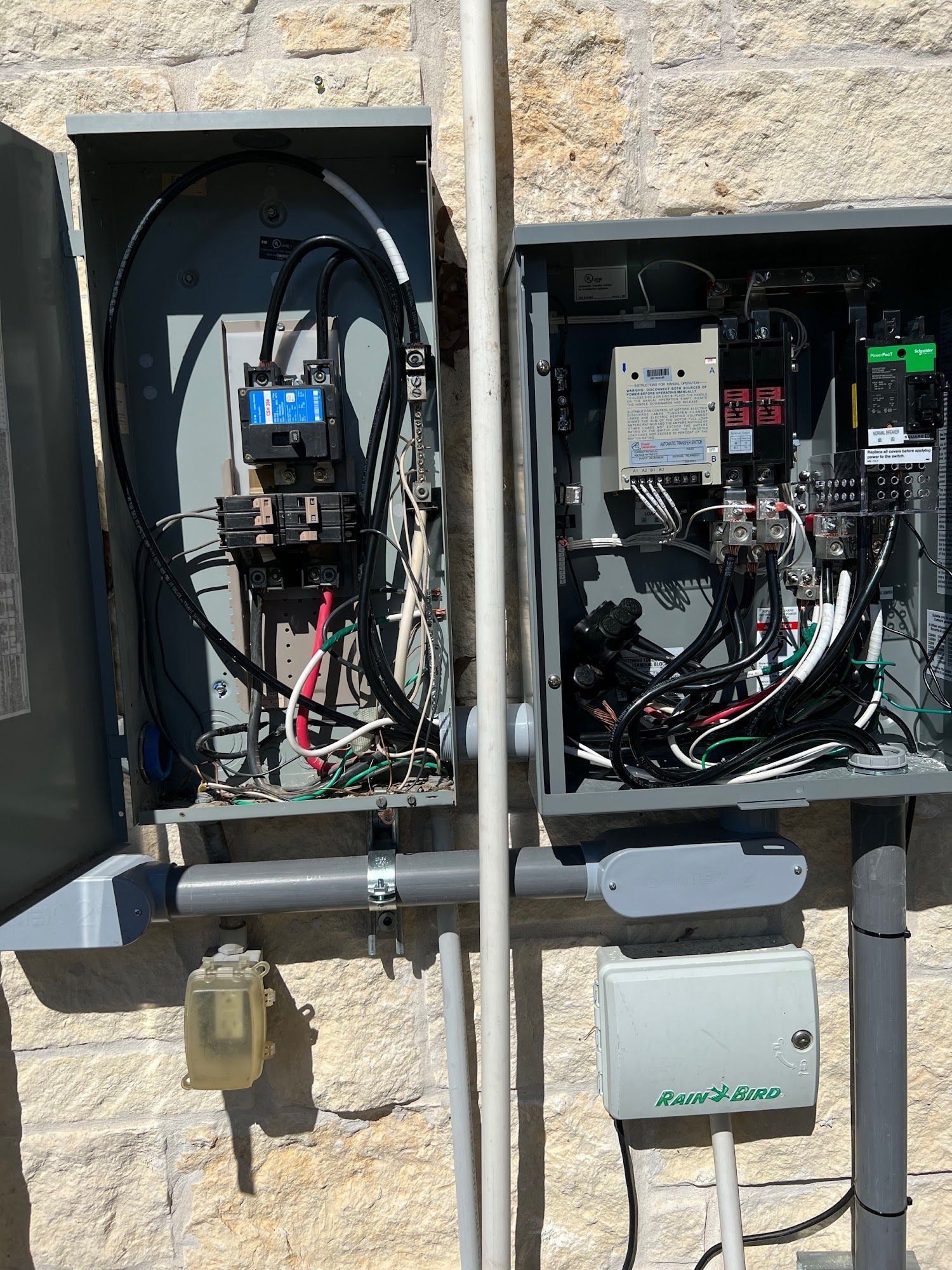 Two open gray electrical boxes on a stone wall, with wires and components visible.