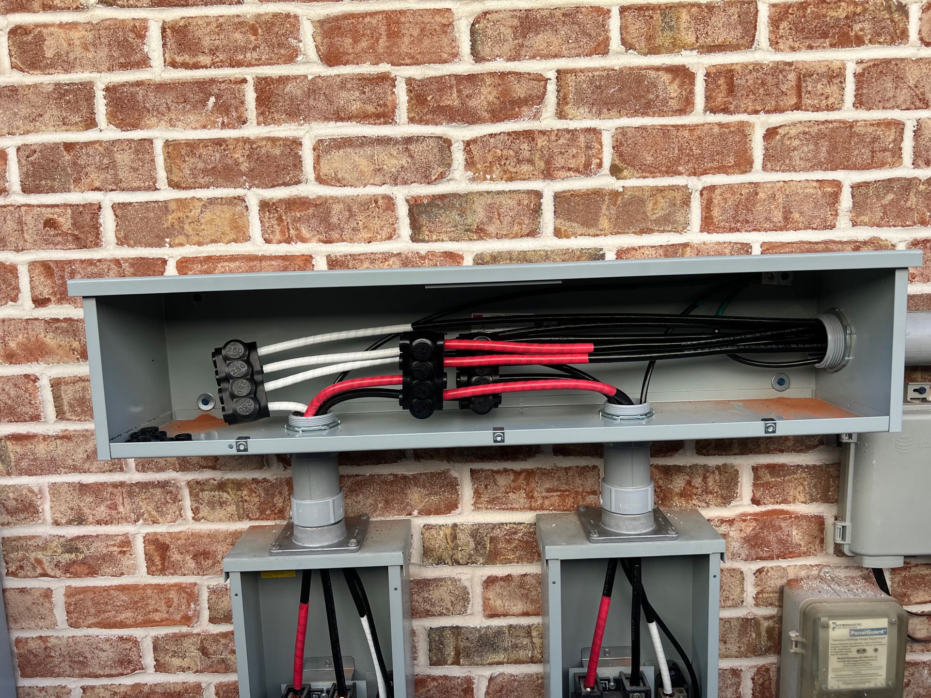 Electrical junction box on brick wall, with wires connected to conduits below.