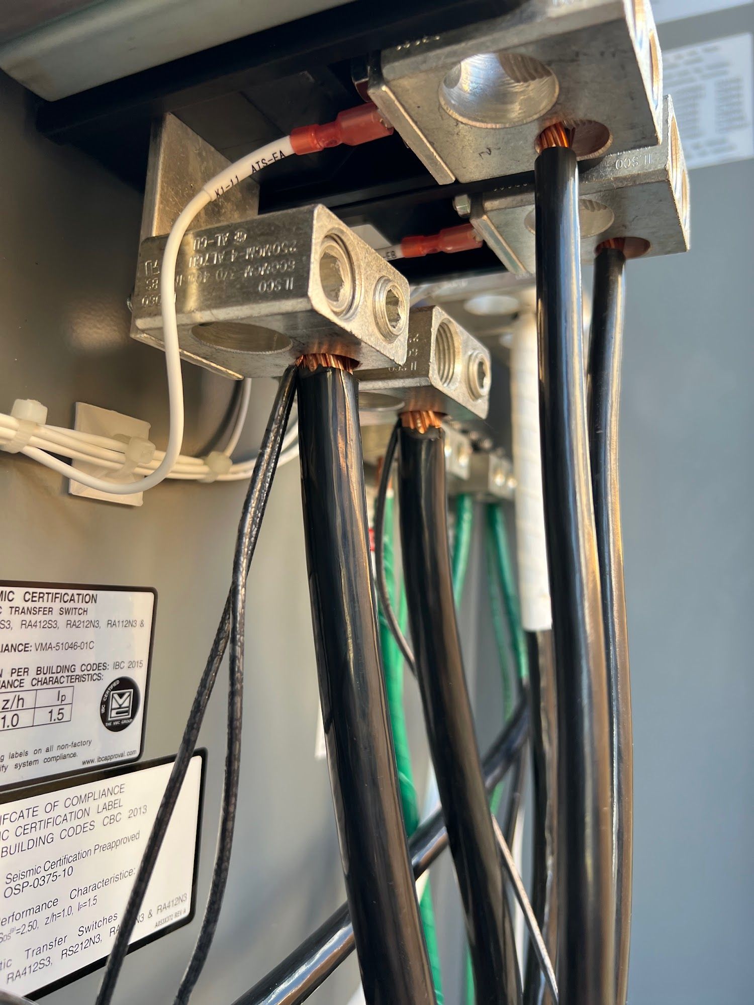 Electrical wiring connected to a metal terminal block inside a gray electrical panel. Black, green, and white wires.