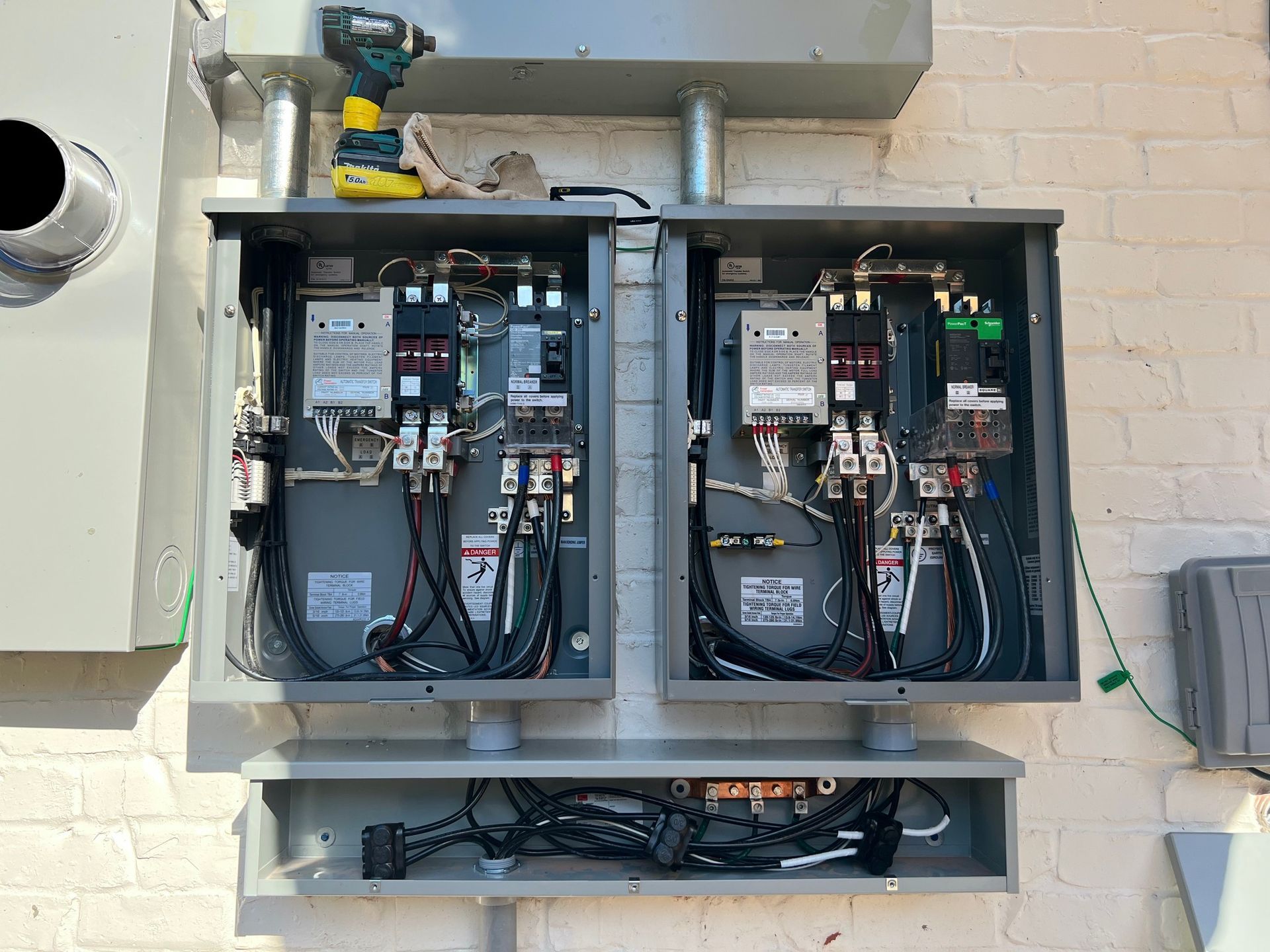 Two open electrical boxes mounted on a brick wall, wires visible inside. A power drill rests on top.