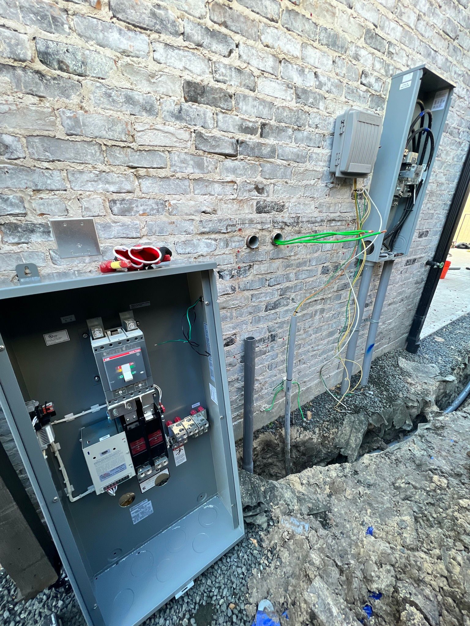 Electrical work in progress: open gray electrical boxes mounted on a brick wall, with exposed wiring and tools nearby.