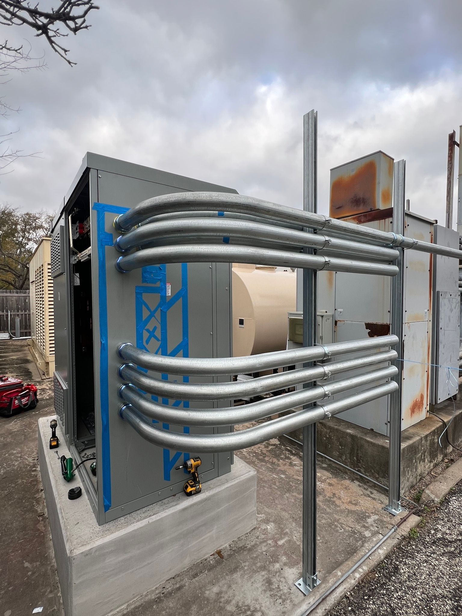 Electrical equipment with conduit, on a concrete base, outdoors, with cloudy sky.