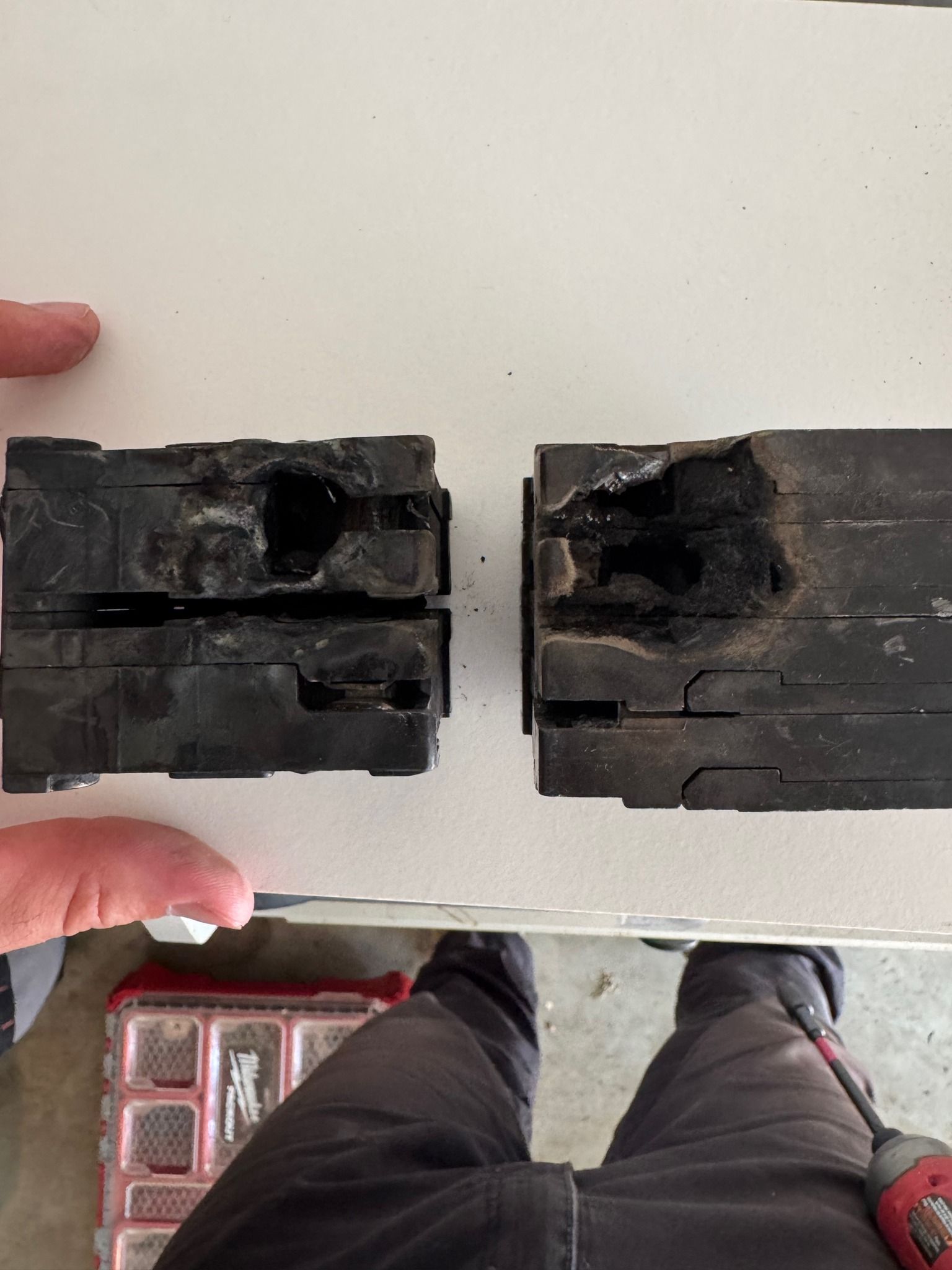 Two severely damaged electrical breakers, burned and charred, lying on a white surface.