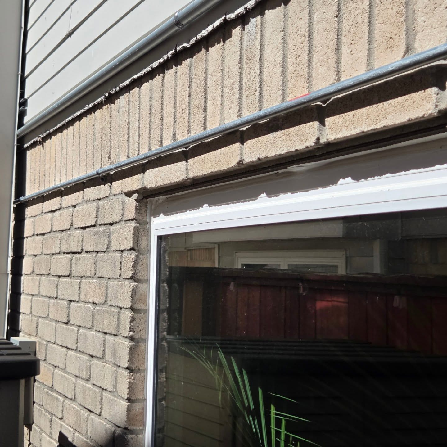 Brick exterior wall with a window below siding and a gutter.