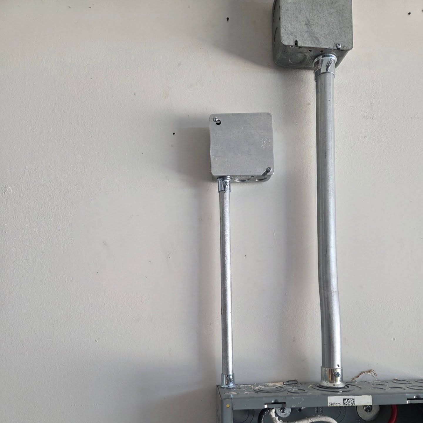 Electrical conduits and boxes mounted on a white wall.
