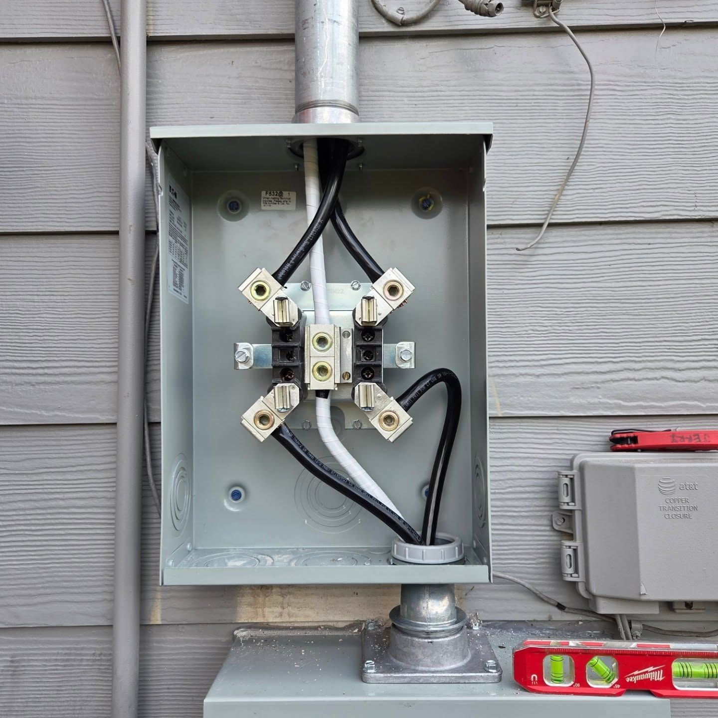Electrical service panel with black and white wires connected to terminals. Gray metal box on siding.
