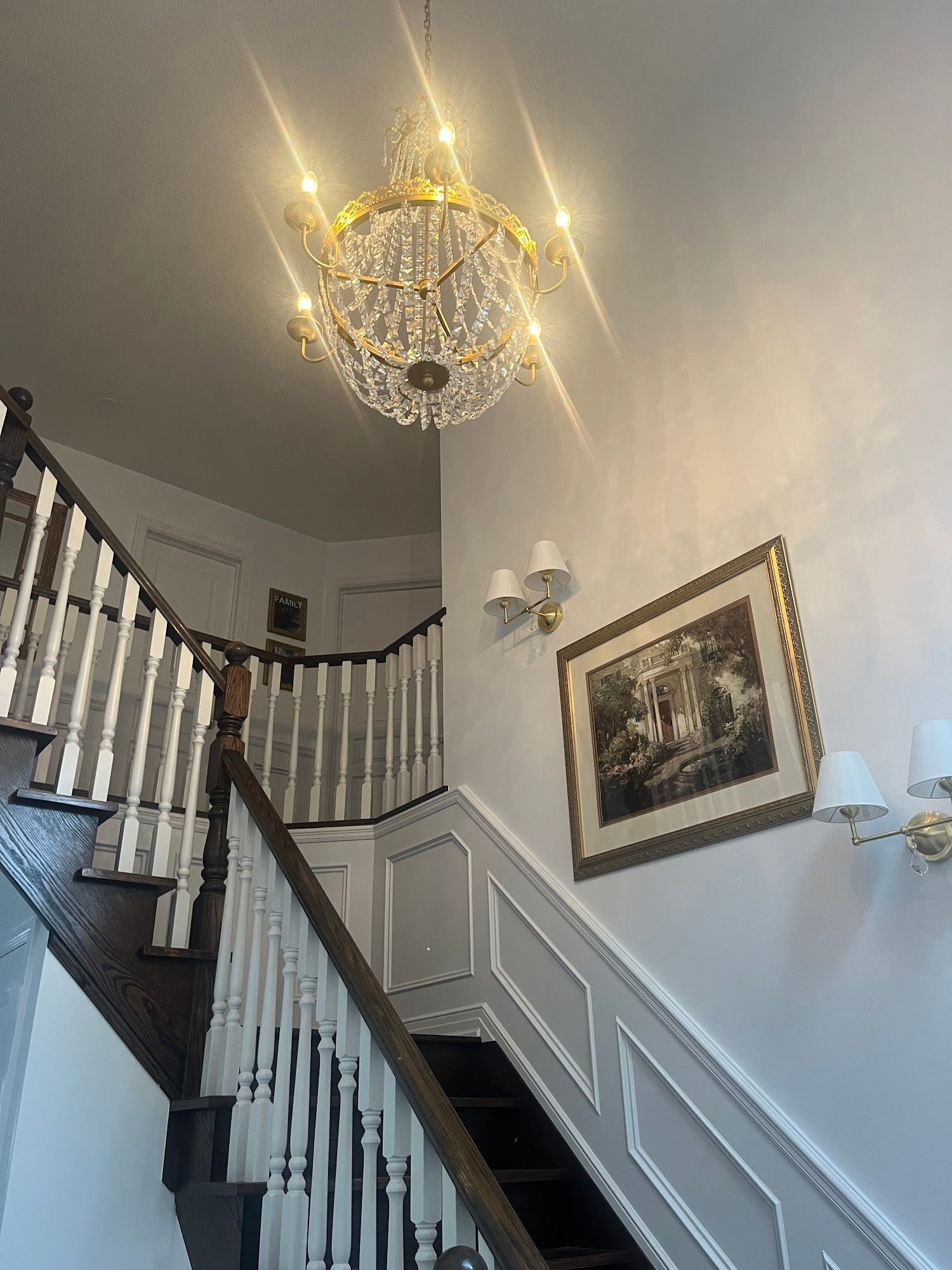 Grand staircase with chandelier, art, and sconces; brown, white, and gold accents.
