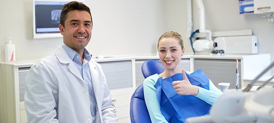 Dentist and patient in a dental office. The patient gives a thumbs up.