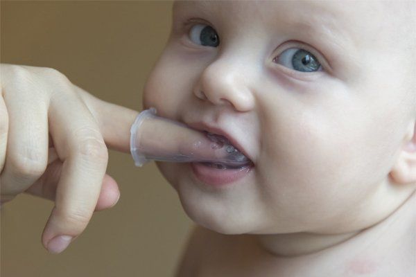 Baby's mouth with finger toothbrush being used. Blue-eyed child with open mouth and finger in mouth.