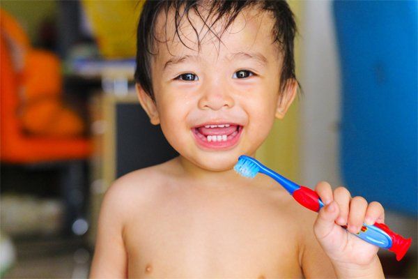 Smiling toddler holding a toothbrush, wet hair, indoors.