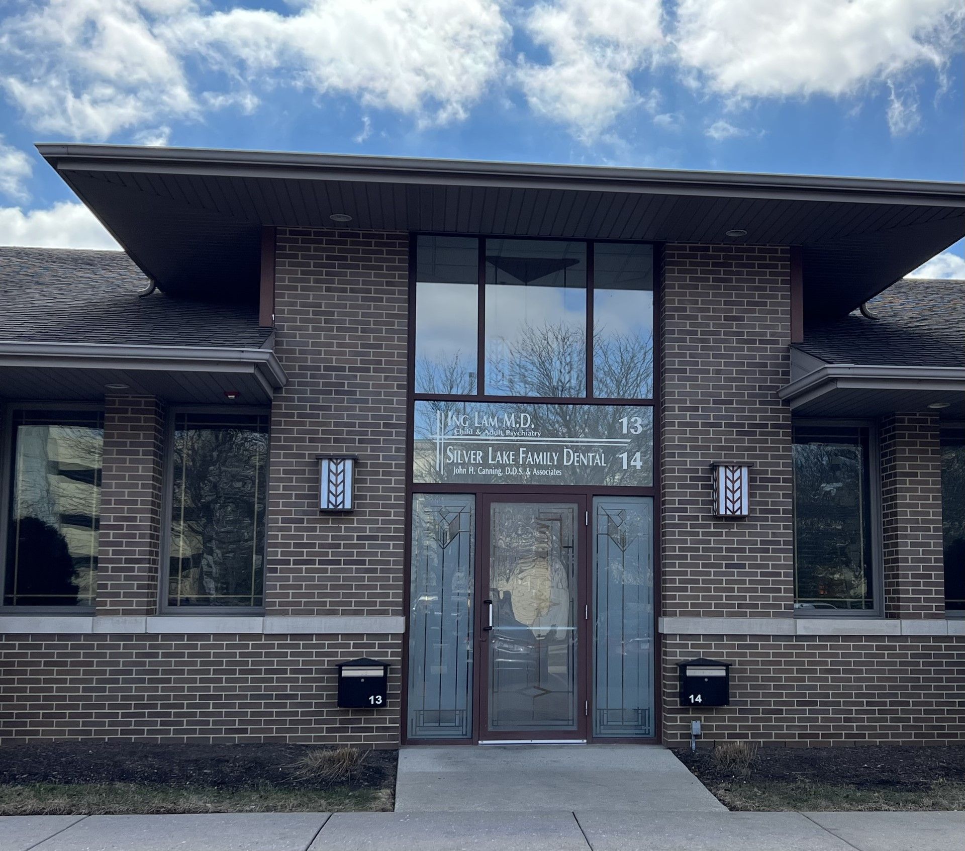 Brick building with large windows and a flat roof under a partly cloudy sky.