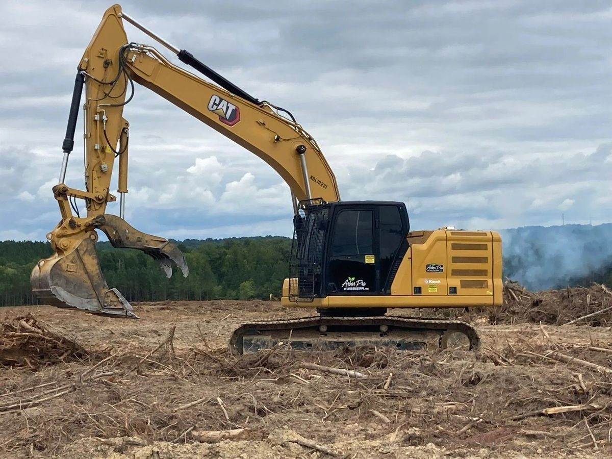 Yellow Caterpillar excavator on cleared land, operating with a grapple attachment.