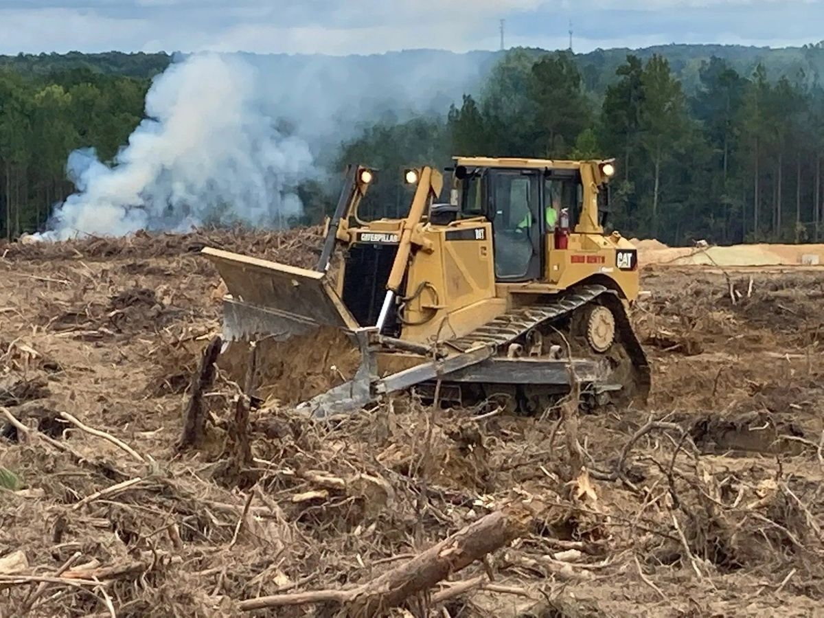 Yellow bulldozer clearing a logged area, smoke in the background.