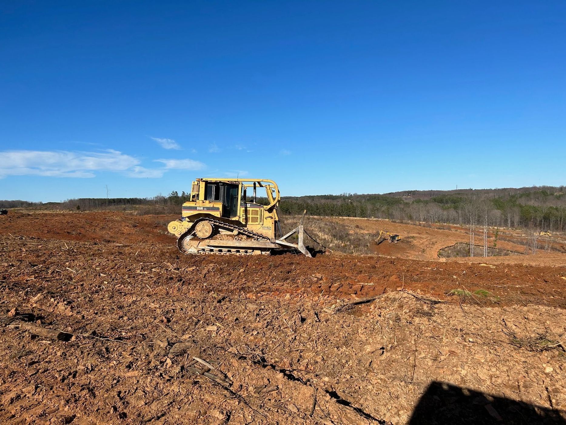 Yellow bulldozer grading a cleared dirt field under a bright blue sky.