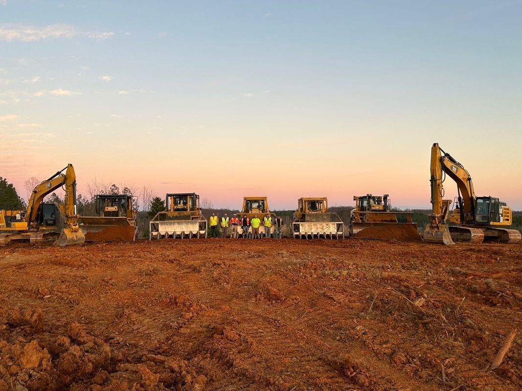 Construction site with excavators and bulldozers on reddish-brown soil at dusk.