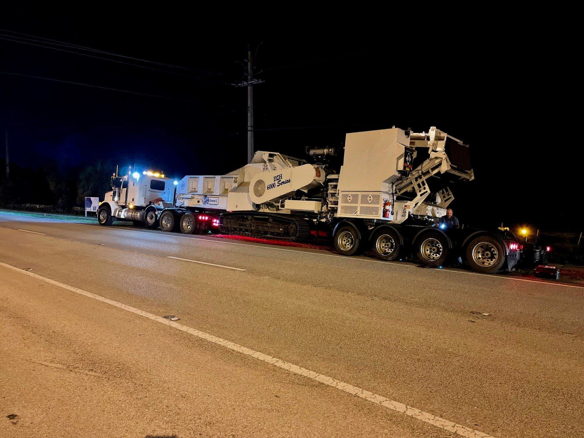 Large truck transporting construction equipment on a road at night.