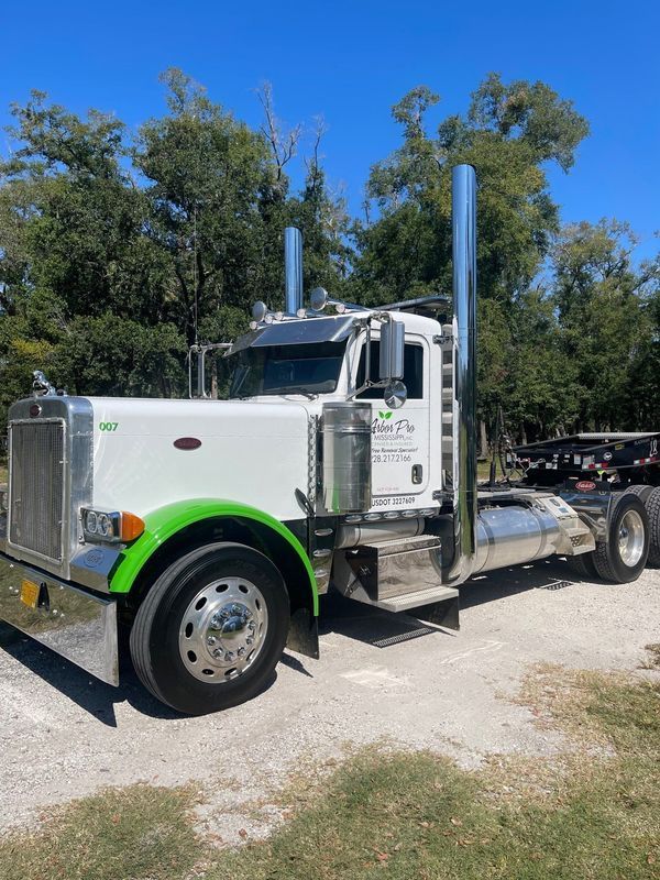 White and green Peterbilt semi truck parked outdoors on a gravel area.