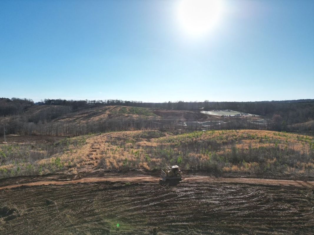Bulldozer clearing land on a sunny day. Hills with sparse trees in the background under a blue sky.