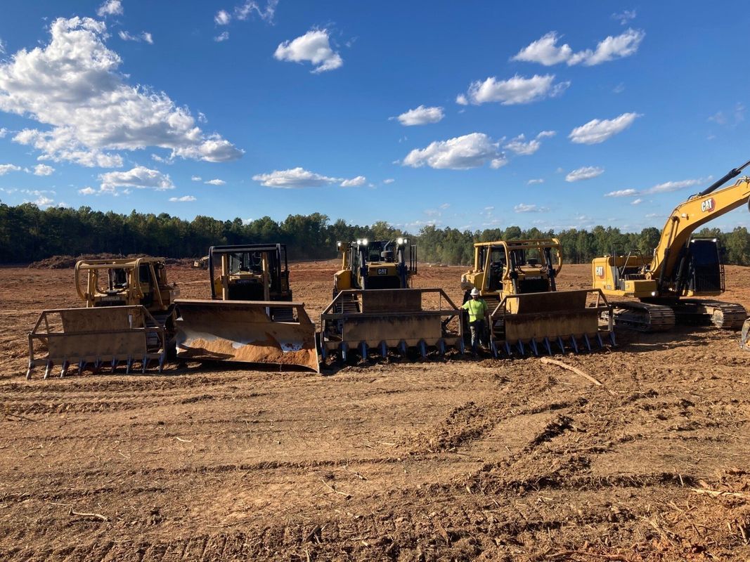 Heavy machinery clearing a field under a blue sky: bulldozers and an excavator.